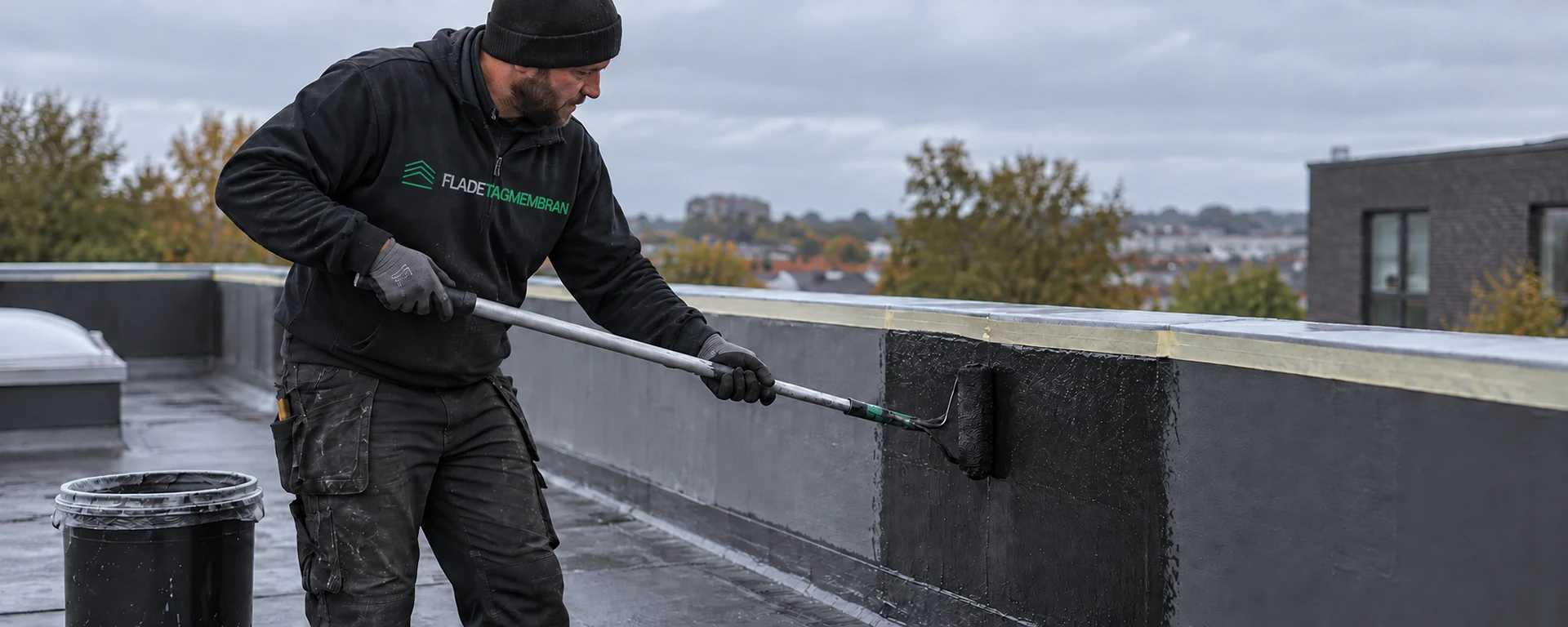 Mand påfører flydende membran ved en opkant på et fladt tag